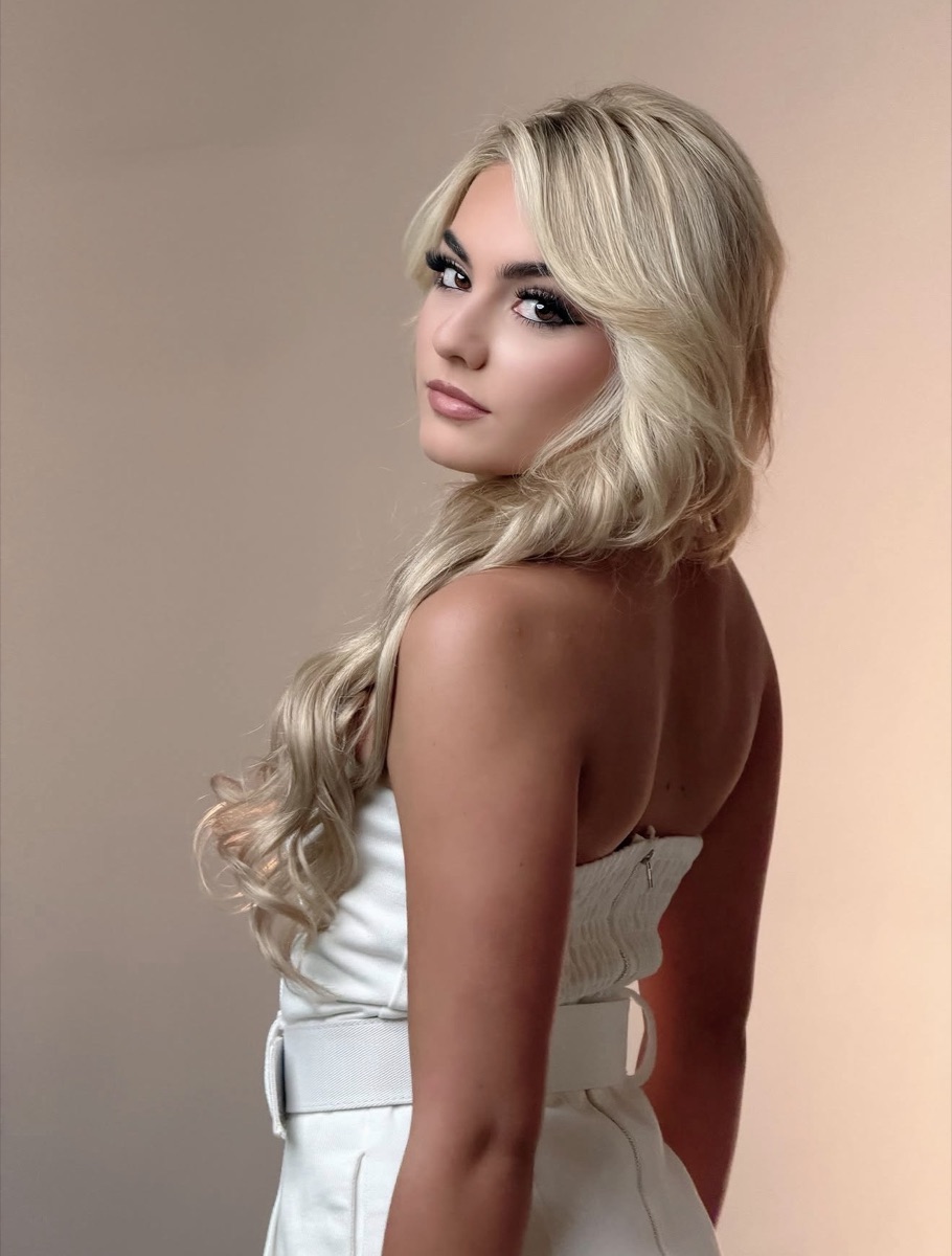 SUPPA looking back over her shoulder in a white strapless dress against a warm beige backdrop