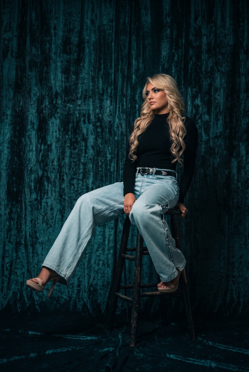 SUPPA seated in front of a teal velvet curtain